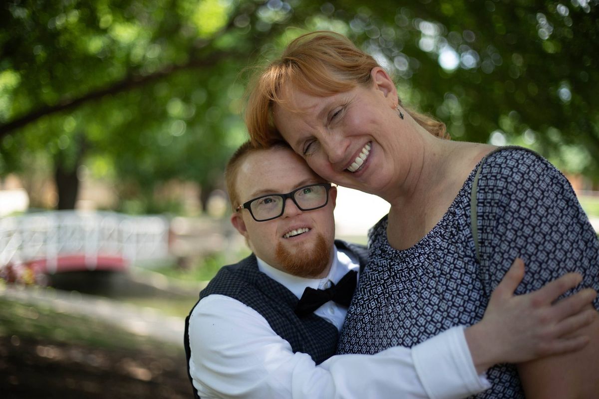 A mother and her adult son share a hug in a park.