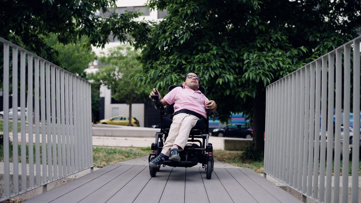 A woman in a power wheelchair crosses a wooden bridge.