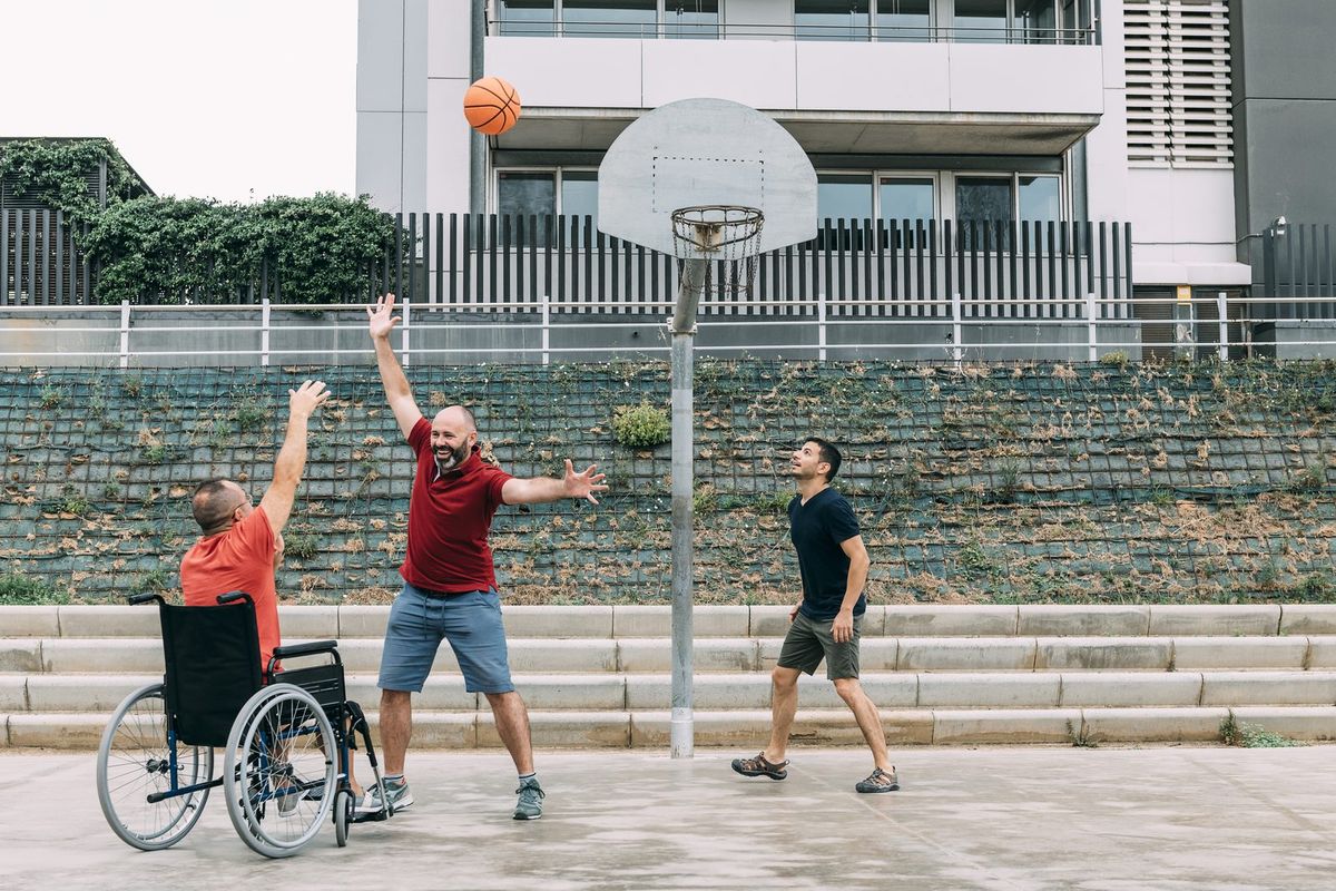 Friends play basketball together, one in a wheelchair.